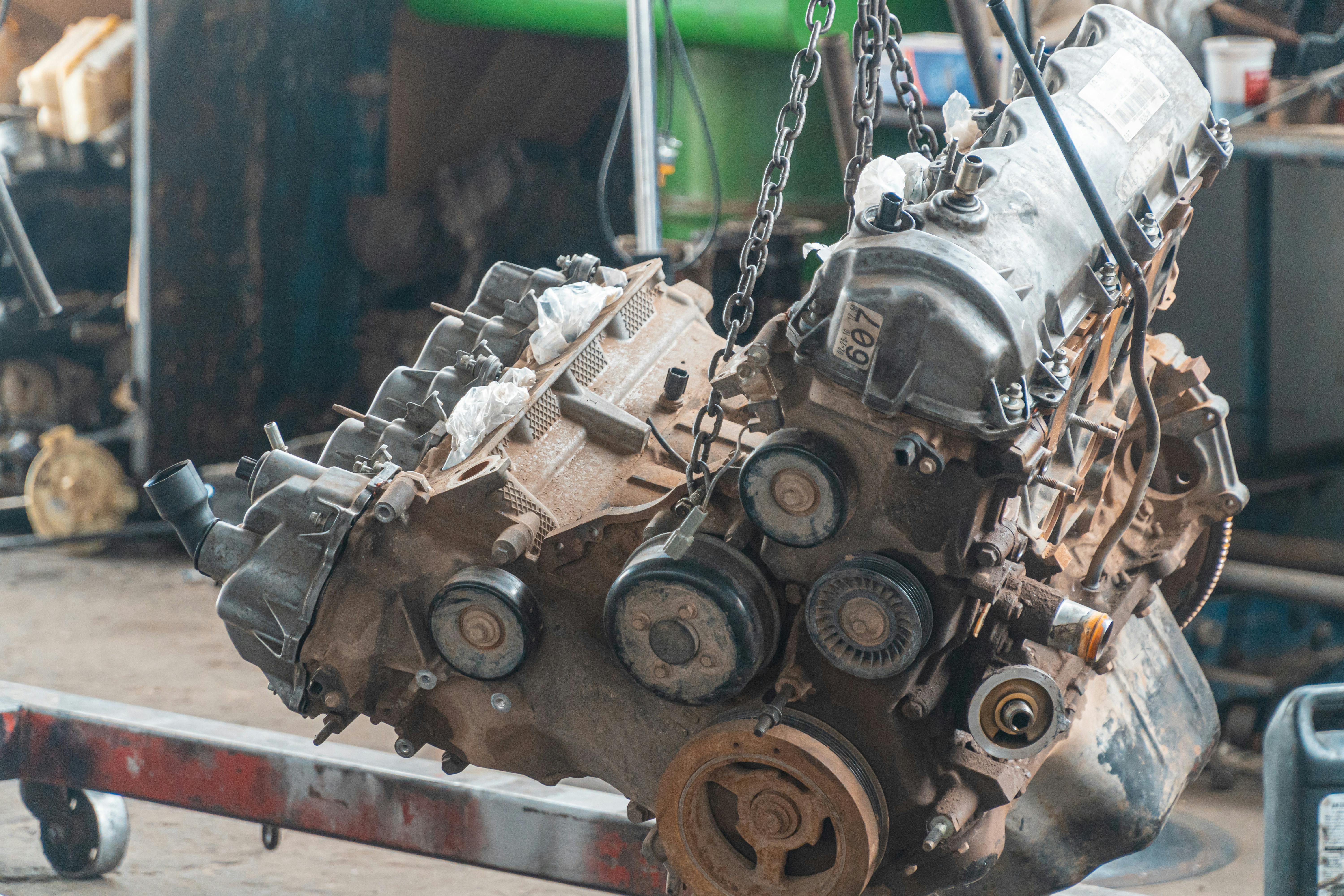Technician lifting a reconditioned engine using a chain hoist in a workshop