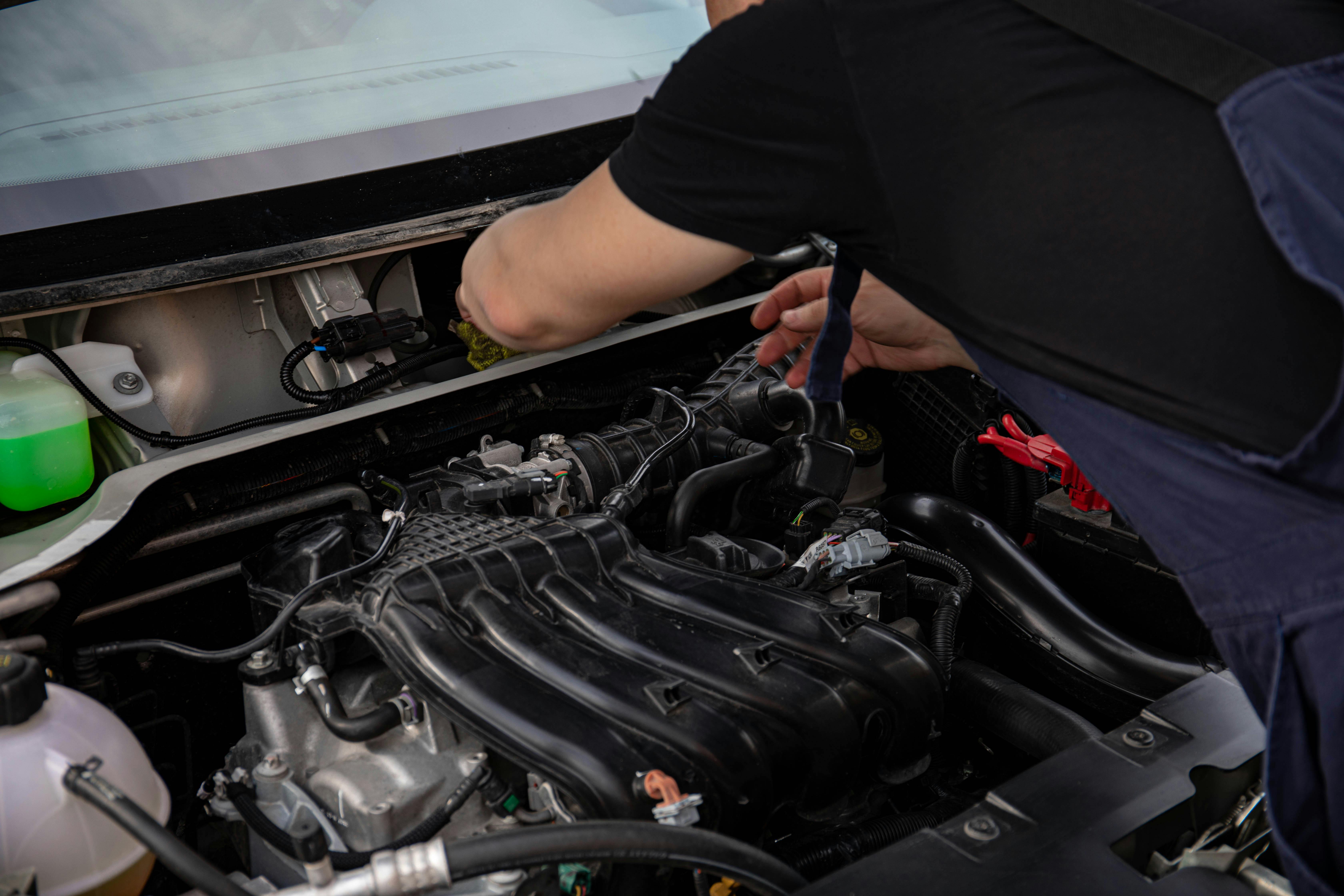 Technician cleaning and maintaining a reconditioned engine inside a car engine bay