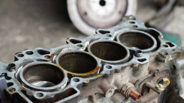 Close-up of a disassembled car engine cylinder block showing four empty cylinders with oil residue and metal components.
